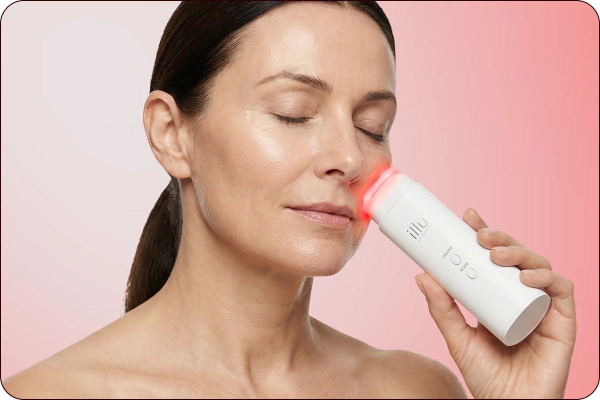 Woman using Illu red light therapy device on cheek to help tighten skin and support a lifted facial appearance.