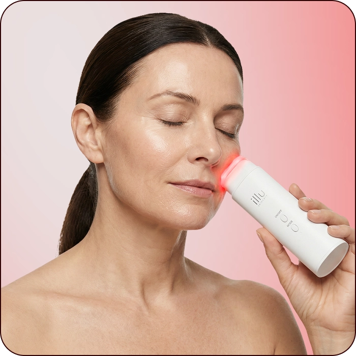 Woman using Illu red light therapy device on cheek to help tighten skin and support a lifted facial appearance.