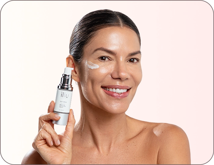 Smiling woman applying ILLU Daily Serum to her face, highlighting hydration, fine line reduction, and radiant daily glow.