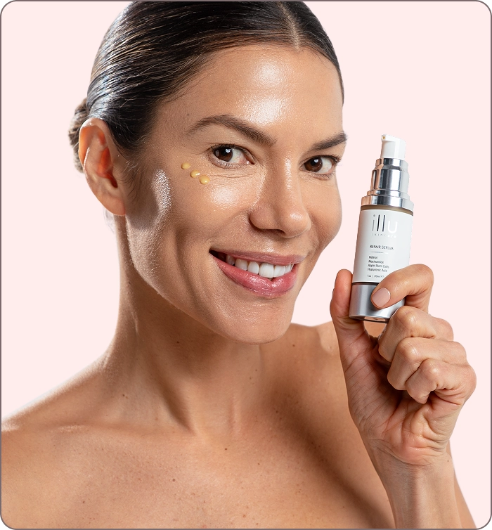 Smiling woman holding ILLU Repair Serum with product applied under her eye, representing firm, luminous skin after consistent use.